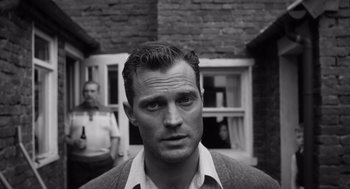 Movie still from “Belfast” (2021), directed by Kenneth Branagh – A black - and - white photo of a man in front of a brick building; Close Up shot, Over the shoulder angle