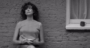 Movie still from “Belfast” (2021), directed by Kenneth Branagh – A black and white photo of a woman sitting against a brick wall; Medium shot, Low angle