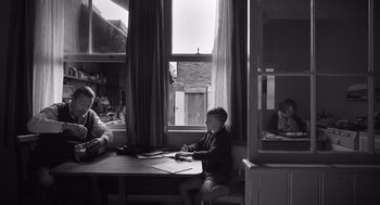 Movie still from “Belfast” (2021), directed by Kenneth Branagh – A young boy sitting at a table in front of a window; Wide shot, Over the shoulder angle