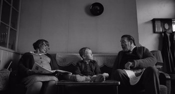 Movie still from “Belfast” (2021), directed by Kenneth Branagh – A black and white photo of a man and woman and a boy sitting on a couch; Wide shot, High angle