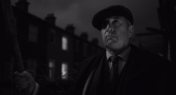 Movie still from “Belfast” (2021), directed by Kenneth Branagh – A black and white photo of a man wearing a hat and tie; Medium shot, Low angle