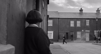 Movie still from “Belfast” (2021), directed by Kenneth Branagh – An older woman walking down the street in a black and white photo; Wide shot, Over the shoulder angle