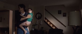 Movie still from “Take Shelter” (2011), directed by Jeff Nichols – A man holding a little girl in his arms in a living room; Medium shot, Low angle
