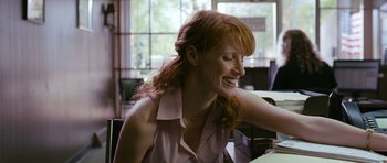 Movie still from “Take Shelter” (2011), directed by Jeff Nichols – A woman sitting at a table with a smile on her face; Medium shot, Low angle