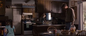 Movie still from “Take Shelter” (2011), directed by Jeff Nichols – A woman sitting at a kitchen counter preparing food; Wide shot, Over the shoulder angle