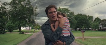Movie still from “Take Shelter” (2011), directed by Jeff Nichols – A man holding a little girl in his arms while walking down the street; Medium shot, Low angle