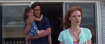 Movie still from “Take Shelter” (2011), directed by Jeff Nichols – A man holding a girl in his arms while a woman looks on; Medium shot, Low angle