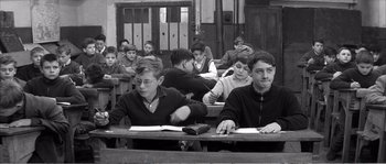 Movie still from “The 400 Blows” (1959), directed by François Truffaut – A black and white photo of a group of people sitting at a table; Medium shot, High angle