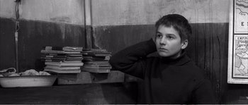 Movie still from “The 400 Blows” (1959), directed by François Truffaut – A young boy leaning against a pile of books; Close Up shot, High angle