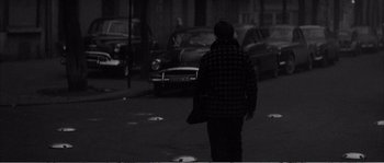 Movie still from “The 400 Blows” (1959), directed by François Truffaut – A person walking down a street with cars in the background at night; Wide shot, High angle