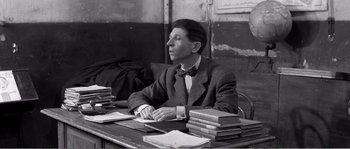 Movie still from “The 400 Blows” (1959), directed by François Truffaut – A black and white photo of a man sitting at a desk; Medium shot, Low angle