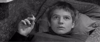 Movie still from “The 400 Blows” (1959), directed by François Truffaut – A young boy laying in bed with a cigarette in his mouth; Close Up shot, High angle