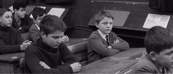 Movie still from “The 400 Blows” (1959), directed by François Truffaut – Two young boys sitting at a table with their arms crossed; Medium shot, High angle