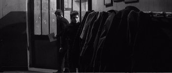 Movie still from “The 400 Blows” (1959), directed by François Truffaut – A man standing in front of a row of jackets; Medium shot, Over the shoulder angle