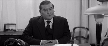 Movie still from “The 400 Blows” (1959), directed by François Truffaut – Black and white photograph of a man sitting at a table; Medium shot, High angle