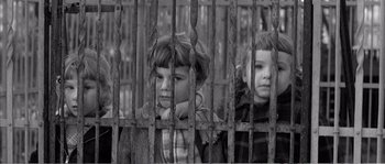 Movie still from “The 400 Blows” (1959), directed by François Truffaut – Two young children behind a metal fence looking at the camera; Medium shot, High angle