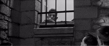Movie still from “The 400 Blows” (1959), directed by François Truffaut – A man looking out of a window through bars; Medium shot, High angle