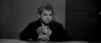 Movie still from “The 400 Blows” (1959), directed by François Truffaut – A young man sitting at a table with his hands crossed; Medium shot, High angle