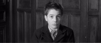 Movie still from “The 400 Blows” (1959), directed by François Truffaut – A young man wearing a suit and tie in front of a wooden wall; Close Up shot, High angle