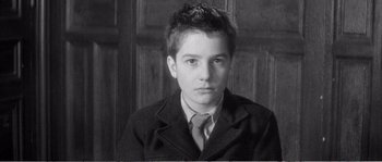 Movie still from “The 400 Blows” (1959), directed by François Truffaut – A young man wearing a suit and tie in front of a wooden wall; Close Up shot, High angle