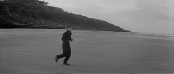 Movie still from “The 400 Blows” (1959), directed by François Truffaut – A man running on the beach with a mountain in the background; Wide shot, High angle