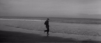Movie still from “The 400 Blows” (1959), directed by François Truffaut – A man walking on the beach near the water; Wide shot, High angle