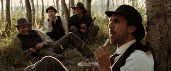 Movie still from “The Assassination of Jesse James by the Coward Robert Ford” (2007), directed by Andrew Dominik – A group of men sitting in the woods eating food; Medium shot, Over the shoulder angle