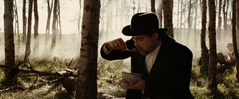 Movie still from “The Assassination of Jesse James by the Coward Robert Ford” (2007), directed by Andrew Dominik – A man wearing a hat eating something in the woods; Medium shot, Low angle