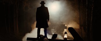 Movie still from “The Assassination of Jesse James by the Coward Robert Ford” (2007), directed by Andrew Dominik – A man in a black coat and hat standing in front of a lantern; Wide shot, Low angle
