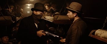 Movie still from “The Assassination of Jesse James by the Coward Robert Ford” (2007), directed by Andrew Dominik – A man in a hat is holding a gun and another man in a hat is holding a gun; Medium shot, Over the shoulder angle