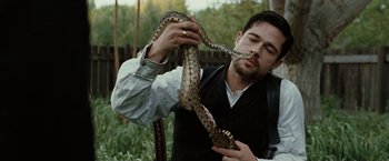 Movie still from “The Assassination of Jesse James by the Coward Robert Ford” (2007), directed by Andrew Dominik – A man holding a snake up to his face; Close Up shot, Low angle