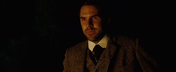 Movie still from “The Assassination of Jesse James by the Coward Robert Ford” (2007), directed by Andrew Dominik – A man wearing a suit and tie in the dark; Close Up shot, Over the shoulder angle