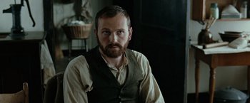 Movie still from “The Assassination of Jesse James by the Coward Robert Ford” (2007), directed by Andrew Dominik – A man with a goatee sitting in a chair; Close Up shot, Over the shoulder angle