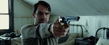 Movie still from “The Assassination of Jesse James by the Coward Robert Ford” (2007), directed by Andrew Dominik – A man holding a gun in a room; Close Up shot, Low angle