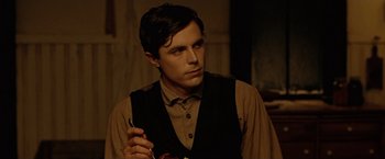 Movie still from “The Assassination of Jesse James by the Coward Robert Ford” (2007), directed by Andrew Dominik – A man in a brown shirt and black vest holding a pair of scissors; Close Up shot, Over the shoulder angle