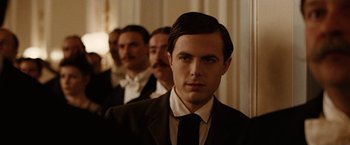 Movie still from “The Assassination of Jesse James by the Coward Robert Ford” (2007), directed by Andrew Dominik – A man in a suit and tie standing in front of a group of other men; Close Up shot, Over the shoulder angle