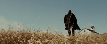 Movie still from “The Assassination of Jesse James by the Coward Robert Ford” (2007), directed by Andrew Dominik – A man in a black coat and a black hat walking through a field; Wide shot, Low angle
