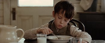 Movie still from “The Assassination of Jesse James by the Coward Robert Ford” (2007), directed by Andrew Dominik – A young boy eating cereal with a fork and a glass of milk; Close Up shot, High angle
