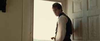 Movie still from “The Assassination of Jesse James by the Coward Robert Ford” (2007), directed by Andrew Dominik – A man standing in front of a window holding a knife; Medium shot, Low angle