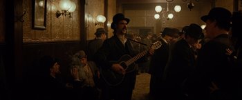 Movie still from “The Assassination of Jesse James by the Coward Robert Ford” (2007), directed by Andrew Dominik – A man with a beard is playing a guitar; Medium shot, Low angle
