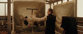 Movie still from “The Assassination of Jesse James by the Coward Robert Ford” (2007), directed by Andrew Dominik – A man holding a paddle in front of a painting; Wide shot, Low angle