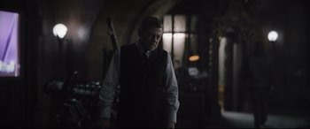 Movie still from “The Batman” (2022), directed by Matt Reeves – A man wearing a vest and tie in a dark room; Medium shot, Over the shoulder angle