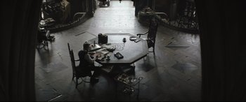 Movie still from “The Batman” (2022), directed by Matt Reeves – A man sitting at a table in a dark room; Wide shot, High angle