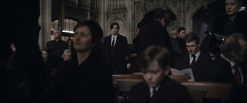 Movie still from “The Batman” (2022), directed by Matt Reeves – A man in a suit and tie standing next to a woman; Medium shot, Over the shoulder angle