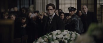 Movie still from “The Batman” (2022), directed by Matt Reeves – A man standing in front of a group of people; Medium shot, Over the shoulder angle