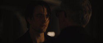 Movie still from “The Batman” (2022), directed by Matt Reeves – A person wearing glasses in a dark room; Close Up shot, Over the shoulder angle