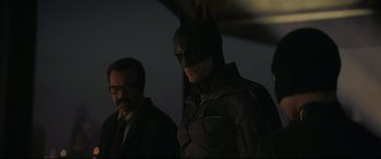 Movie still from “The Batman” (2022), directed by Matt Reeves – A man in a batman suit standing next to another man; Medium shot, Over the shoulder angle