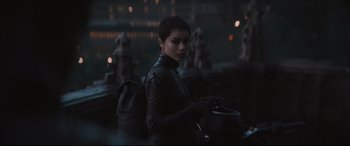 Movie still from “The Batman” (2022), directed by Matt Reeves – A woman in a black leather jacket with a backpack; Medium shot, Over the shoulder angle