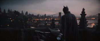 Movie still from “The Batman” (2022), directed by Matt Reeves – A man dressed as batman standing next to a motorcycle in front of a city skyline; Wide shot, Over the shoulder angle
