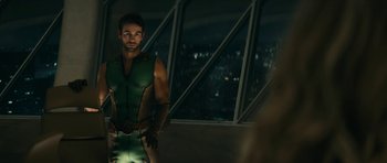 Movie still from “The Boys” (2019), created by Eric Kripke – A man in a green and black outfit standing in front of a window; Medium shot, Over the shoulder angle